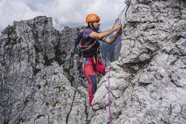 Männlicher Bergsteiger mit Seil beim Klettern am Berg, Europäische Alpen, Lecco, Italien - MCVF00614