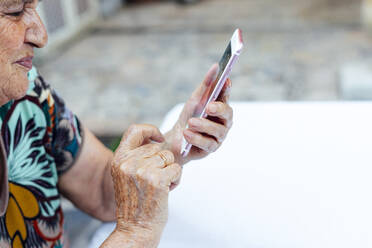 Nahaufnahme einer älteren Frau, die am Tisch im Hof ein Smartphone benutzt - PGF00005