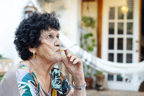 Nahaufnahme einer älteren Frau, die vor einem Haus im Hof sitzt und eine Zigarette raucht - PGF00008