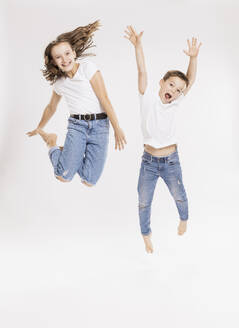 Cheerful siblings jumping against white background - SDAHF00979