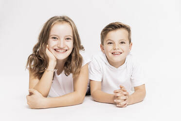 Niedliche lächelnde Geschwister liegend auf weißem Hintergrund - SDAHF00981