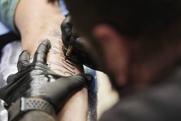 Nahaufnahme eines männlichen Künstlers beim Tätowieren der Hand eines Kunden im Studio - SASF00100