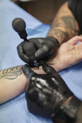 Close-up of male artist tattooing customer's hand on bed in studio - SASF00102