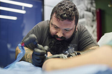 Close-up of bearded artist tattooing on customer's hand in studio - SASF00103