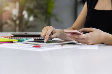 Close-up of businesswoman using digital tablet and smart phone on desk in office - BMOF00443