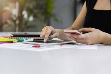 Nahaufnahme einer Geschäftsfrau, die ein digitales Tablet und ein Smartphone auf einem Schreibtisch im Büro benutzt - BMOF00443