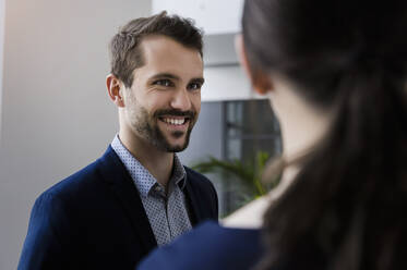 Close-up of smiling businessman discussing with female coworker in office - BMOF00455