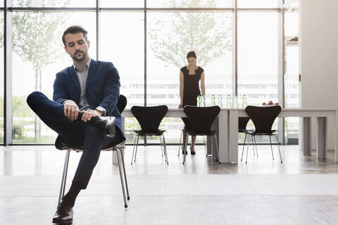 Serious businessman sitting on chair while female coworker working at desk in background stock photo