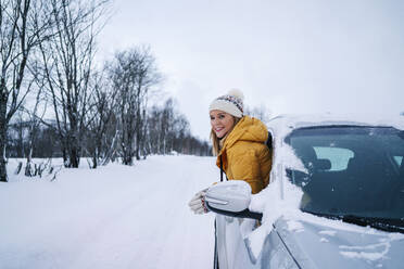 Smiling woman peeking through car window against sky during winter - DGOF01426