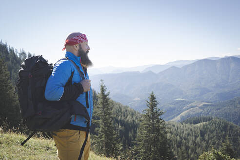 Bärtiger Mann mit Rucksack, der die Aussicht betrachtet, während er auf einem Berg gegen den klaren Himmel steht, Otscher, Österreich - HMEF01061