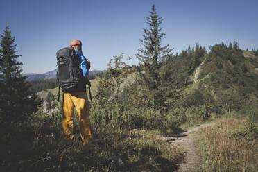 Männlicher Wanderer mit Rucksack steht inmitten von Pflanzen auf einem Berg gegen den klaren Himmel, Otscher, Österreich - HMEF01063