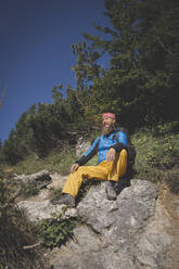Männlicher Wanderer auf einem Berg sitzend gegen den klaren Himmel an einem sonnigen Tag in Otscher, Österreich - HMEF01065