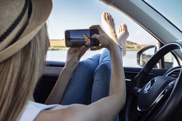 Junge Frau, die im Auto sitzend ihre Füße fotografiert - JSRF01117