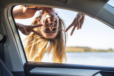 Unbekümmerte Frau zeigt Friedenszeichen, während sie durch ein Autofenster schaut - JSRF01121