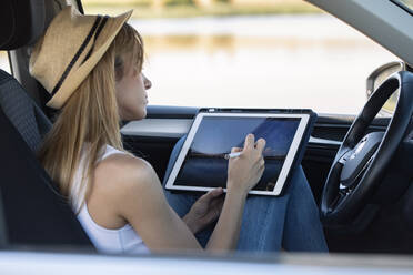 Frau, die im Auto sitzend mit einem digitalen Tablet malt - JSRF01122