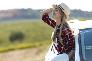 Beautiful woman wearing hat smiling while leaning out of car window - JSRF01128