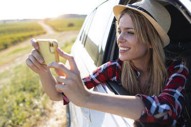 Lächelnde junge Frau, die ein Foto mit ihrem Handy macht, während sie im Auto sitzt - JSRF01132