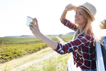 Junge Frau, die ein Selfie mit ihrem Mobiltelefon macht, während sie sich aus dem Autofenster lehnt - JSRF01133