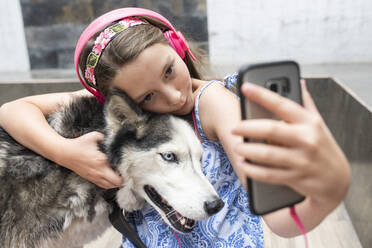 Mädchen mit Kopfhörer nimmt Selfie mit Hund zu Hause - DSIF00136