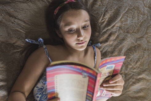 Girl reading book while lying on bed at home - DSIF00138