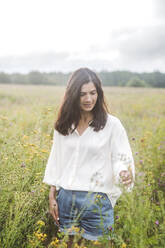 Mid adult woman standing amidst flowers growing in field against sky - EYAF01307