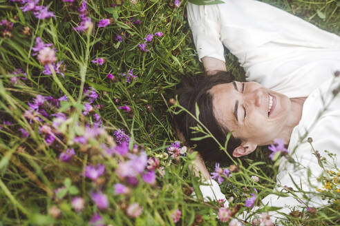 Fröhliche Frau mit geschlossenen Augen inmitten von Pflanzen an Land liegend - EYAF01309