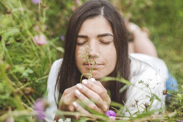 Close-up of mid adult woman with eyes closed smelling flowers while lying on land - EYAF01310