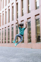 Young man jumping with hand raised on street in city - XLGF00497