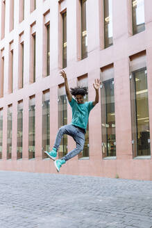 Junger Mann springt mit erhobener Hand auf der Straße in der Stadt - XLGF00497