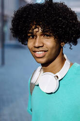 Man standing with headphone in neck on street during sunny day - XLGF00506