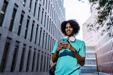 Junger Mann Textnachrichten auf Smartphone stehend gegen Gebäude außen in der Stadt, lizenzfreies Stockfoto