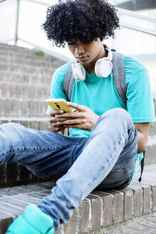 Junger Mann schreibt eine SMS auf seinem Smartphone, während er auf einer Treppe in der Stadt sitzt - XLGF00526