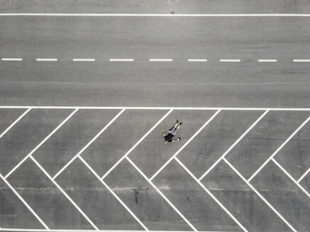 Drohnenansicht eines auf dem Rücken liegenden Mannes auf einem leeren Parkplatz - MEUF02048
