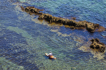 Aerial view of woman paddleboarding in clear water of Lukin bay - KNTF05401