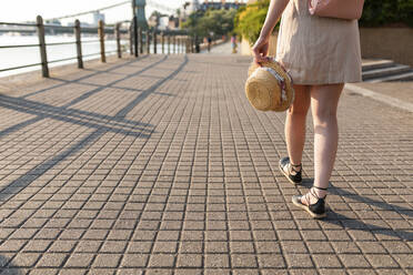 Legs of woman walking on pavement along riverside - WPEF03399
