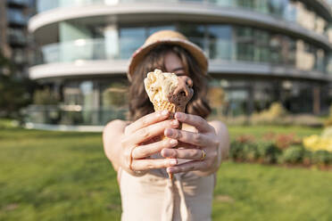 Junge Frau mit Eiscreme in der Hand in einem öffentlichen Park an einem sonnigen Tag - WPEF03401