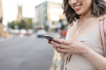 Nahaufnahme einer Frau, die in der Stadt stehend eine SMS auf ihrem Smartphone schreibt - WPEF03408