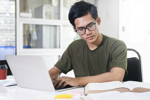 Junger Collegestudent mit Computer und mobilem Gerät beim Lernen - CAVF89234