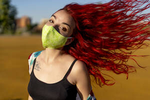 Redhead woman wearing protective face mask while standing outdoors - OCMF01714