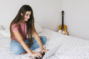 Junge Frau benutzt einen Laptop, während sie zu Hause im Schlafzimmer sitzt - XLGF00533