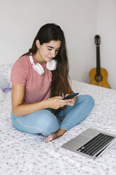 Frau benutzt Smartphone, während sie zu Hause im Schlafzimmer sitzt - XLGF00534