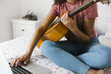 Frau lernt online Gitarre spielen, während sie zu Hause im Schlafzimmer sitzt - XLGF00540