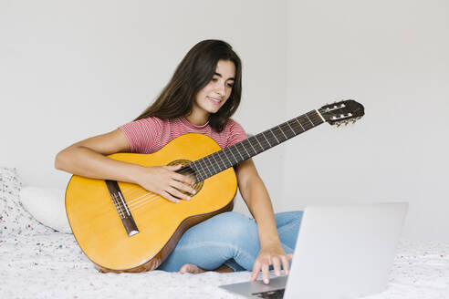 Frau lernt online zu Hause im Schlafzimmer Gitarre - XLGF00541