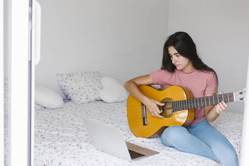 Junge Frau lernt online Gitarre, während sie zu Hause im Schlafzimmer sitzt - XLGF00542