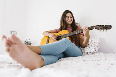 Smiling young woman playing guitar at home in bedroom - XLGF00543