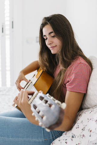 Junge Frau spielt zu Hause im Schlafzimmer Gitarre, lizenzfreies Stockfoto