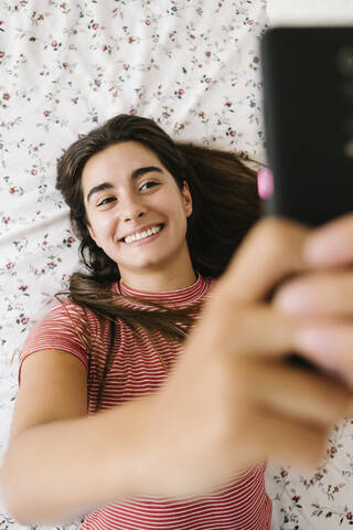 Lächelnde Frau nimmt Selfie auf Smartphone im Schlafzimmer, lizenzfreies Stockfoto