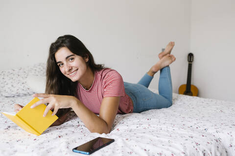 Young woman reading book while lying down on bed at home stock photo