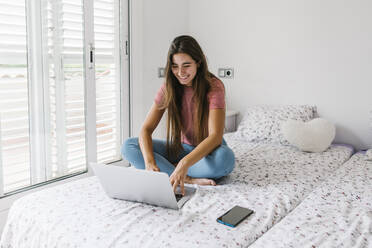 Junge Frau studiert am Laptop, während sie zu Hause im Schlafzimmer sitzt - XLGF00564