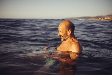 Mann schwimmt bei Sonnenuntergang im Meer - MEUF02066